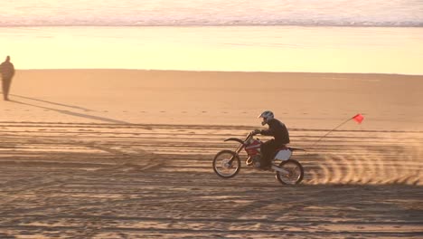 un motociclista hace huellas en una playa de arena durante la hora dorada