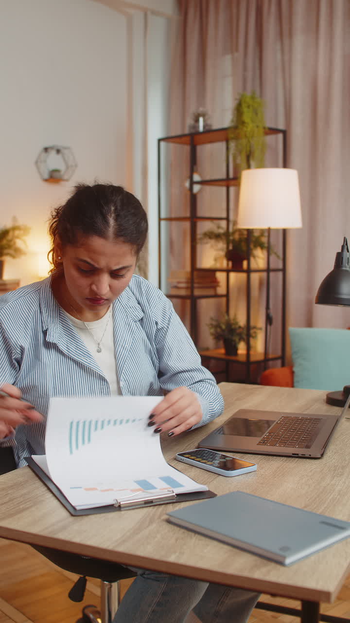 Indian woman working with financial graphs calculate taxes for charts and reports at desk at home
