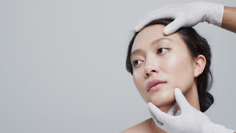 hands in gloves touching face of asian woman on grey background with copy space, slow motion