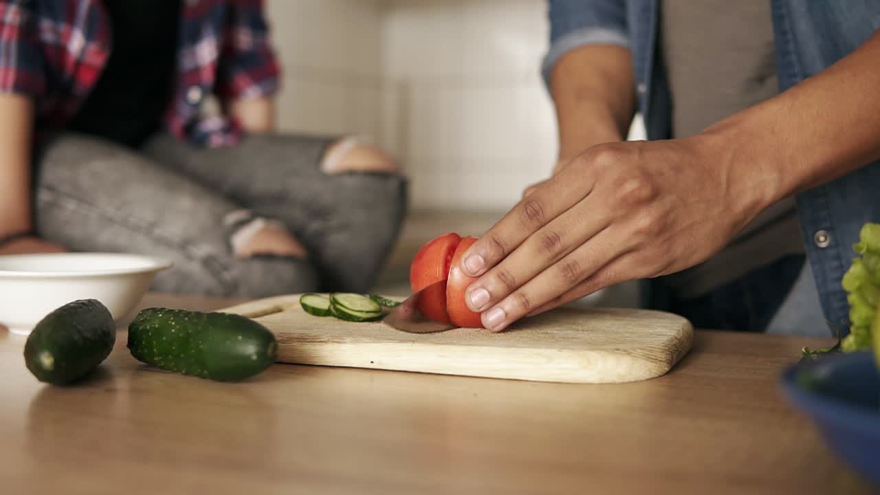 슬로우 모션 클로즈업으로 젊은 유쾌한  ⁇ 라토 남자가  ⁇ 러드에 토마토를 자르고, 그의 여자친구와 함께 점심을 준비하고 있습니다. 관계 목표.
