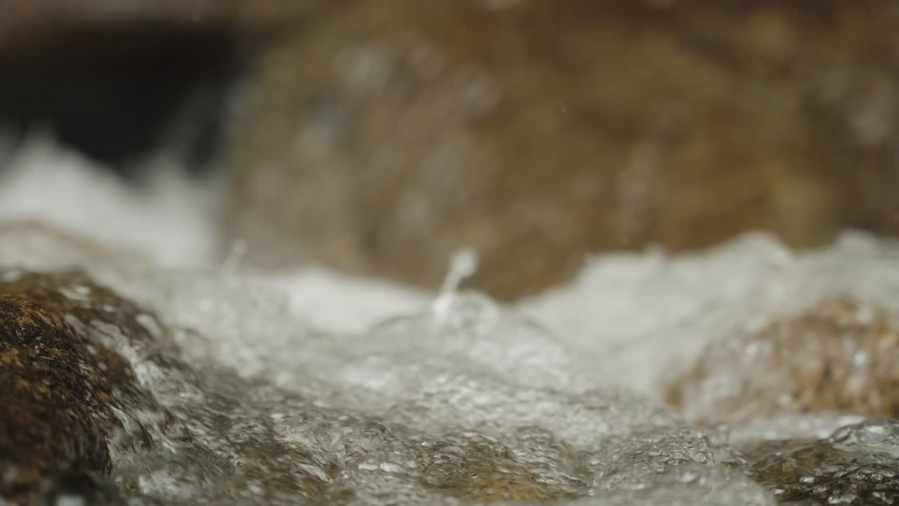 Super slowmo macro detail shot of water splashing through river with droplets 120fps