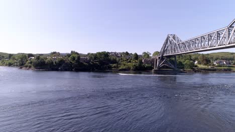 Aerial-push-in-shot-of-a-speed-boat-moving-quickly-underneath-the-Connel-Bridge,-near-Oban