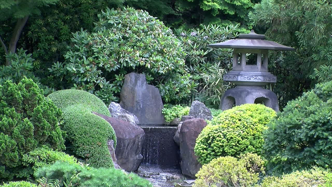 Una lanterna in pietra si erge accanto a una cascata in un giardino giapponese.