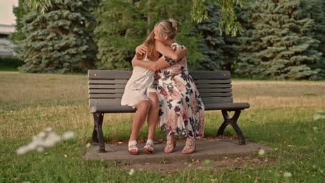 a young adult daughter talks with her mother on a park bench before sharing a warm emotional hug filled with trust and affection captured in a smooth dolly to the right in natural light