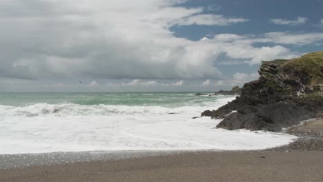 Costa-Escarpada-Y-Olas-Rompiendo-En-La-Playa-Con-Nubes-Pasando-Sobre-Un-Cielo-Azul-En-Cámara-Lenta