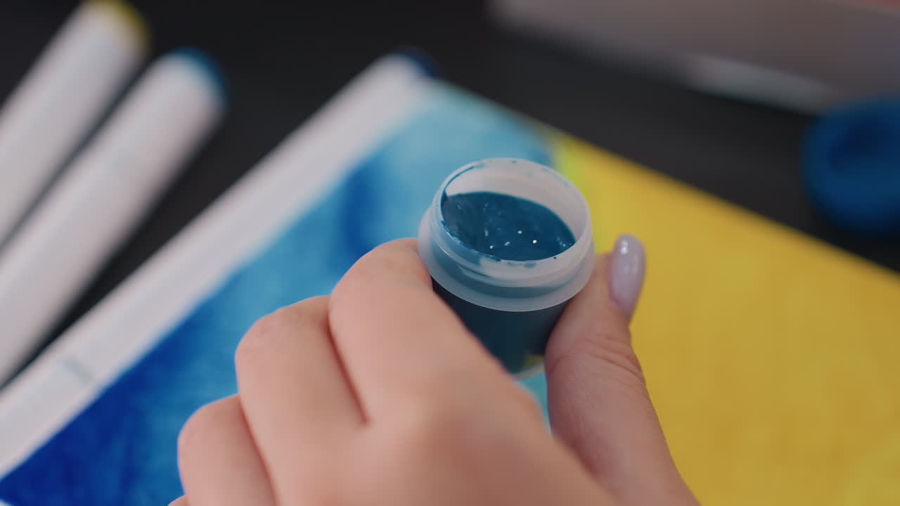 Mujer inspeccionando pintura, mujer examinando un color azul vibrante, mujer analizando un pigmento azul brillante en un recipiente, mujer mirando dentro de una lata abierta de pintura azul celeste brillante para evaluar su calidad