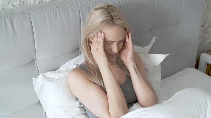 wanita duduk di tempat tidur memegang kepalanya dia memiliki sakit kepala yang menyakitkan