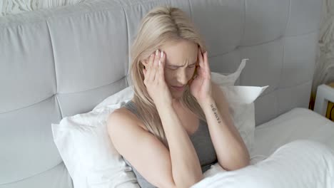 women sitting on bed holding her head  she has a painful headache