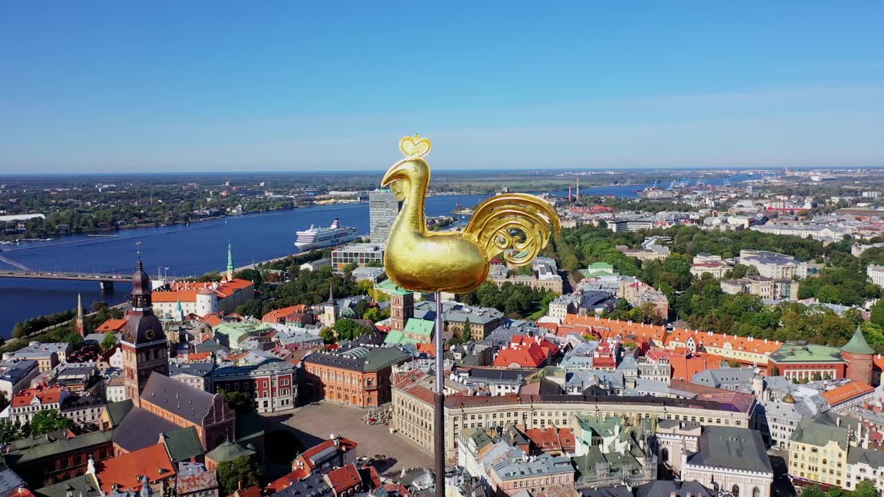 Iconic weathercock symbol stands over rooftops and bridge, bright Baltic summer