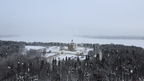 pazailis monastery in lithuania covered in snow during snowfall, aerial ascend view