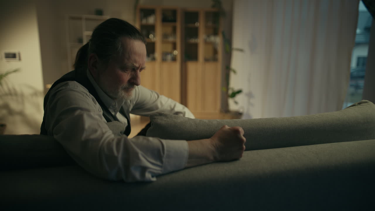 Distressed Senior Man Clenching Fist on Sofa