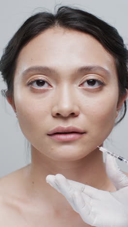 vertical video of giving injection in lip of asian woman on grey background, slow motion