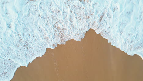 top view of splashing sea waves wetting the beach sand and very white foam