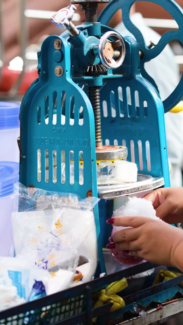 Close-up of a vendor operating a vintage blue manual ice shaver for street food.