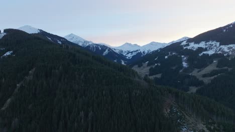 Schneebedeckte-Gipfel-überragen-Die-üppigen-Kiefernwälder-Von-Saalbach-Hinterglemm-In-Der-Abenddämmerung,-Luftaufnahme