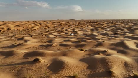 the drone is flying forward looking at a white car driving through the sahara desert in tunisia aerial footage 4k