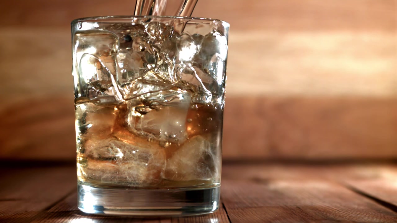 Whisky dorato versato su ghiaccio in un bicchiere su un tavolo di legno