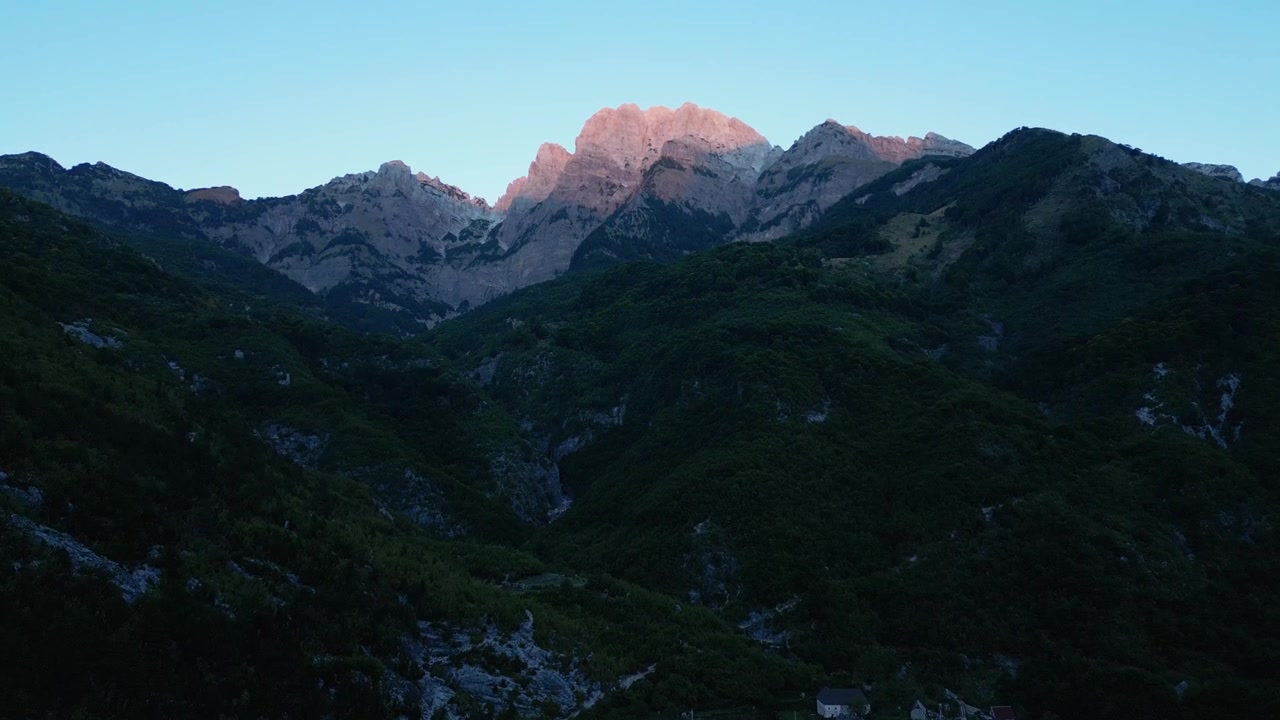 Riprese drone delle montagne di Theth al crepuscolo, con gli ultimi raggi del tramonto che illuminano le aspre cime delle Alpi Albanesi. Mostra paesaggi alpini mozzafiato, natura selvaggia e bellezza naturale.