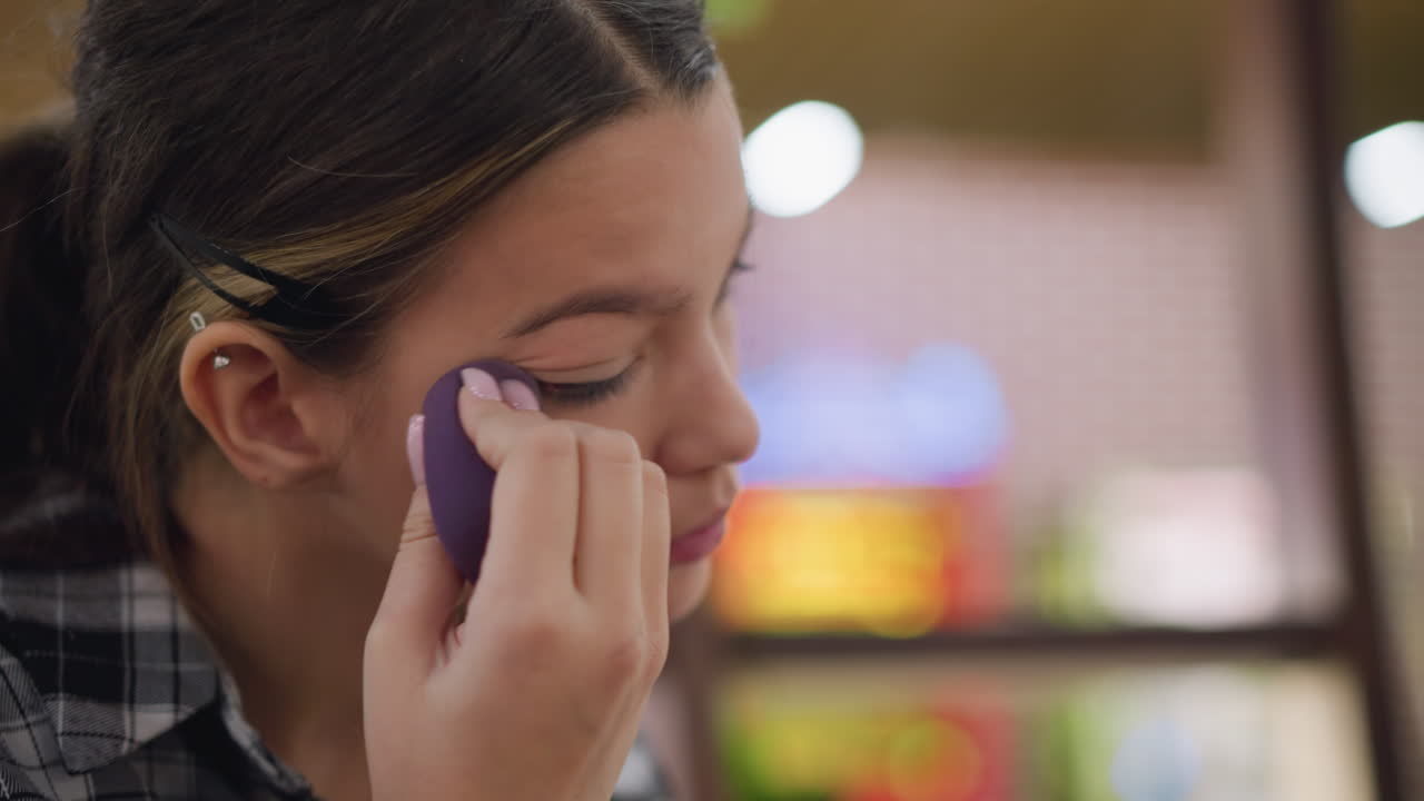 primer plano de una joven mezclando cuidadosamente el maquillaje al lado del ojo derecho usando esponja de belleza para un acabado sin costuras, mejora de la complexión suave con una aplicación precisa, iluminación suave y fondo borroso