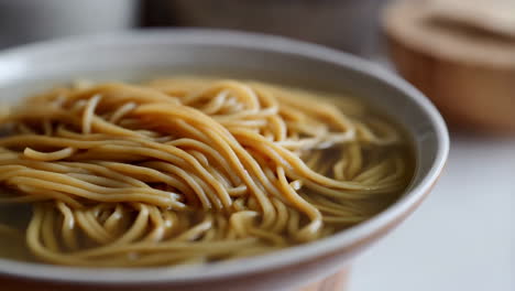 a close-up view of a bowl of plain noodles submerged in clear broth