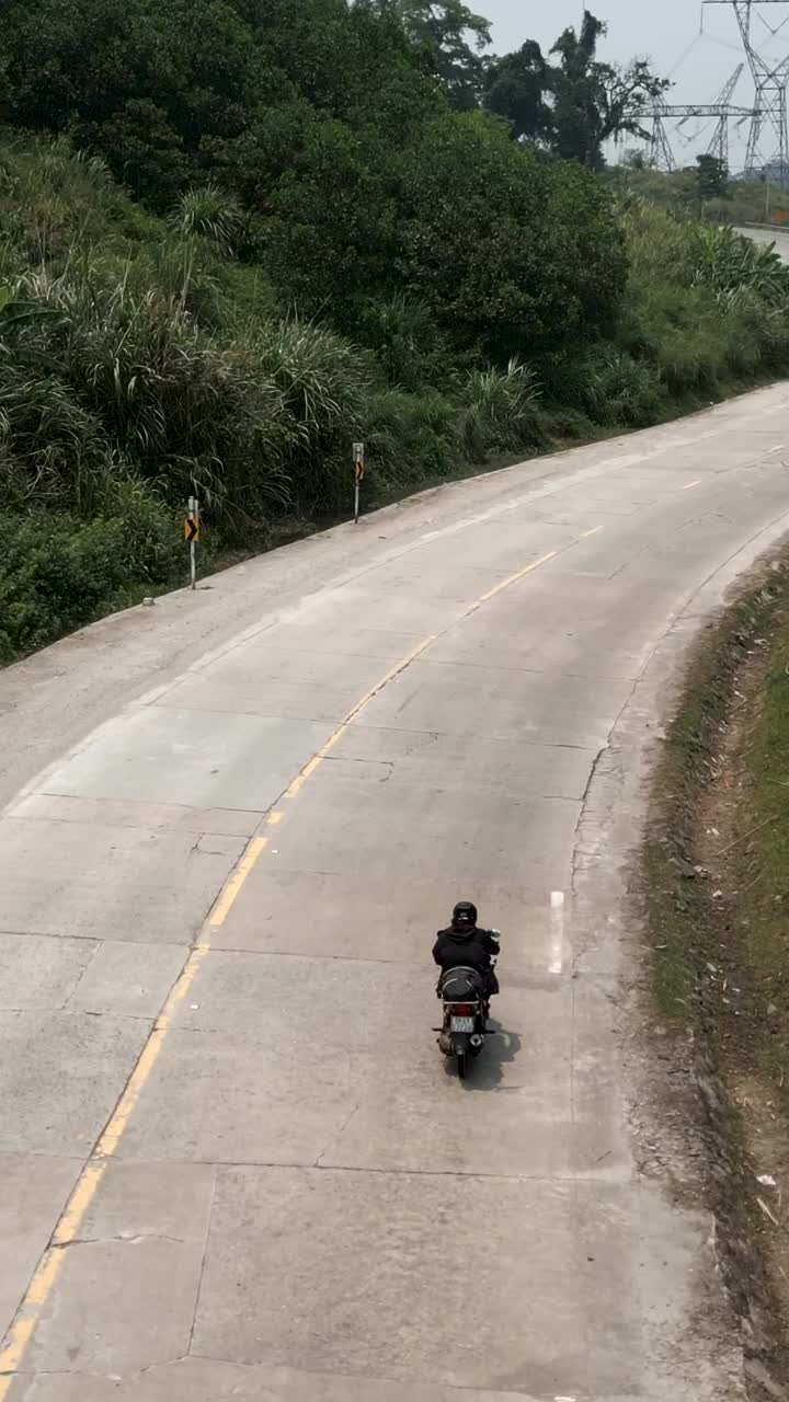 A motorcyclist rides on a winding road through a rural landscape
