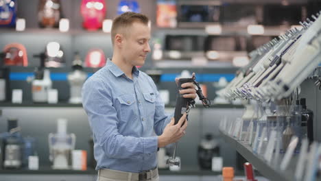 a man chooses a blender in the appliances store kitchen appliances in his hands and considers the design and characteristics