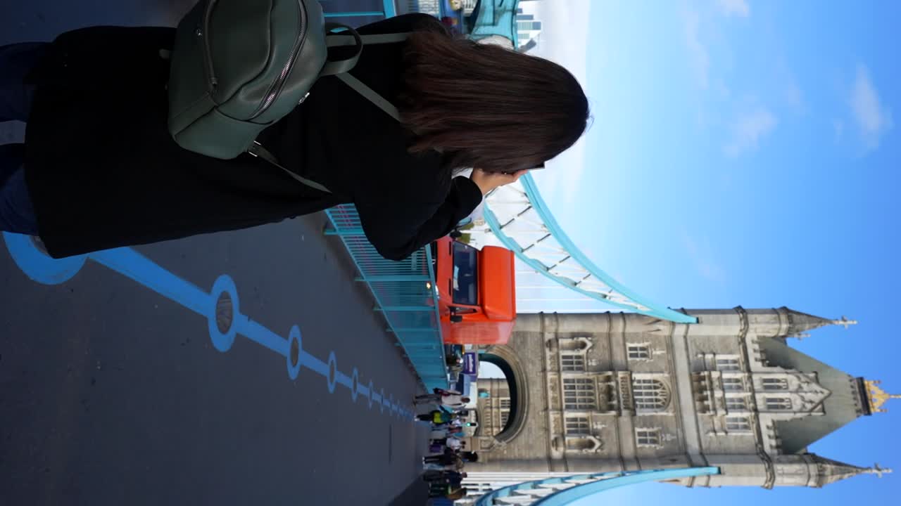 Woman photographing Tower Bridge in London on a sunny day with cars passing by