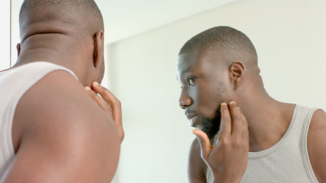 Man examining face in mirror, grooming at home spa for skincare routine