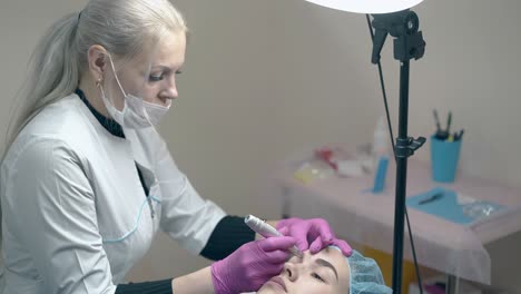 la esteticista con bata blanca hace maquillaje permanente en la ceja