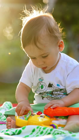 nice cute baby boy plying on the plaid outdoors. beautiful child touching bright toys with interest. bright sun at backdrop. vertical video