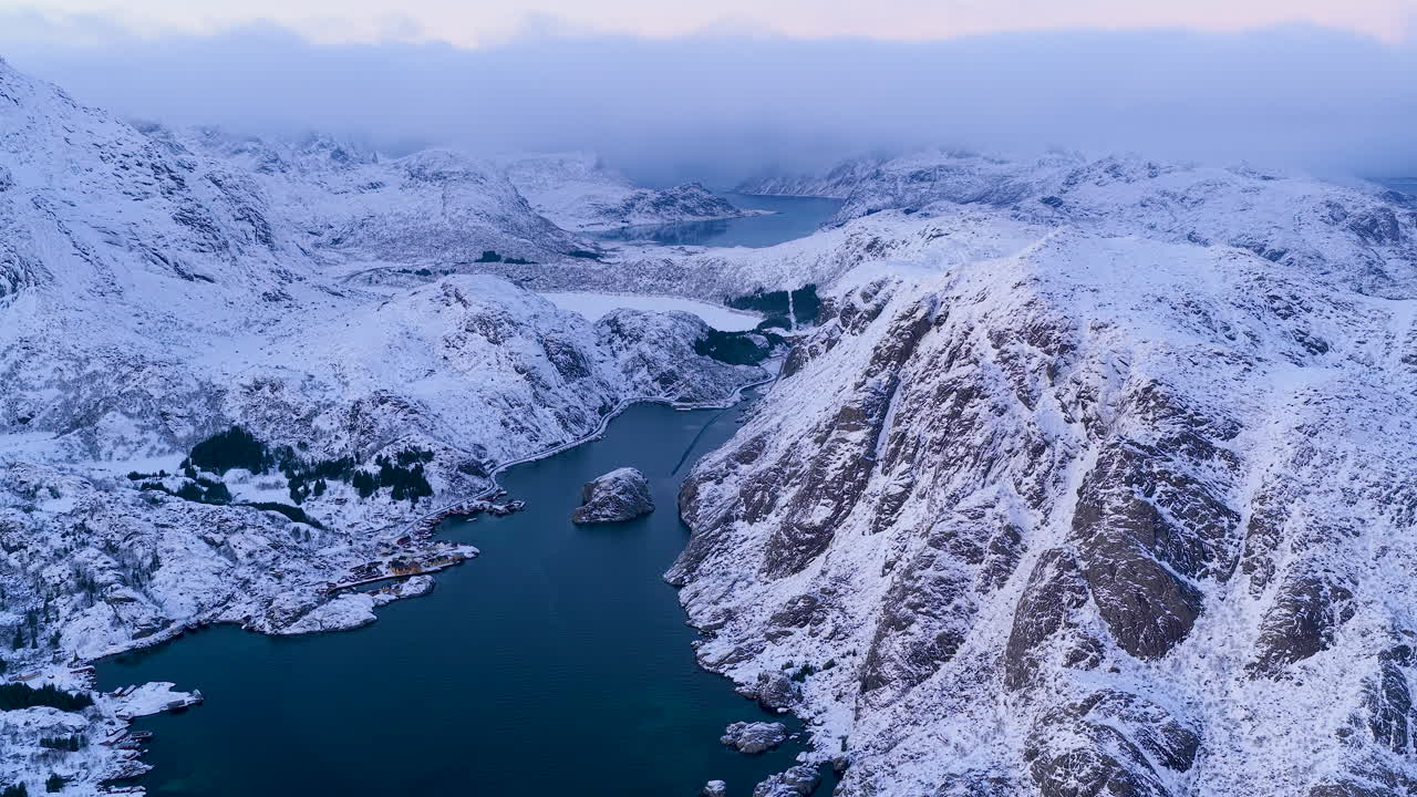 Dechberoucí letecký záběr zasněžených horských štítů a hlubokých modrých fjordů na Lofotech v Norsku. Ideální pro cestopisné dokumenty a obsah o přírodním wellness.
