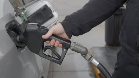 gas station white caucasian man with wedding ring filling up silver car removing inserted gas nozzle from tank and turning towards pump with rain or snow falling