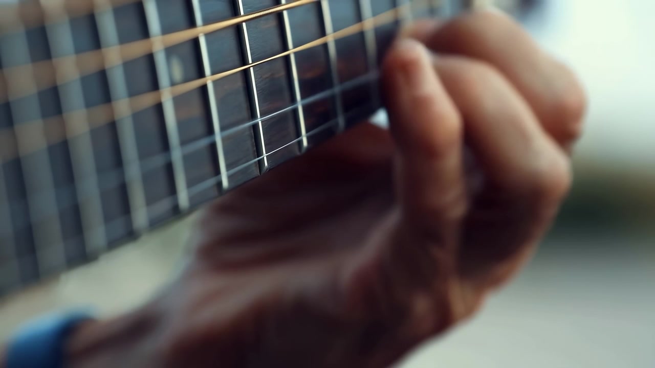 Close-up view of a hand plucking guitar strings on the fretboard, with shallow focus, soft natural light, and a blurred background that emphasizes the