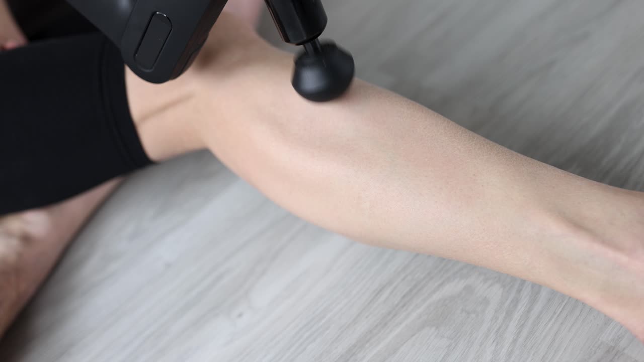 Donna che massaggia la gamba con un massaggiatore a percussione, video 4K.