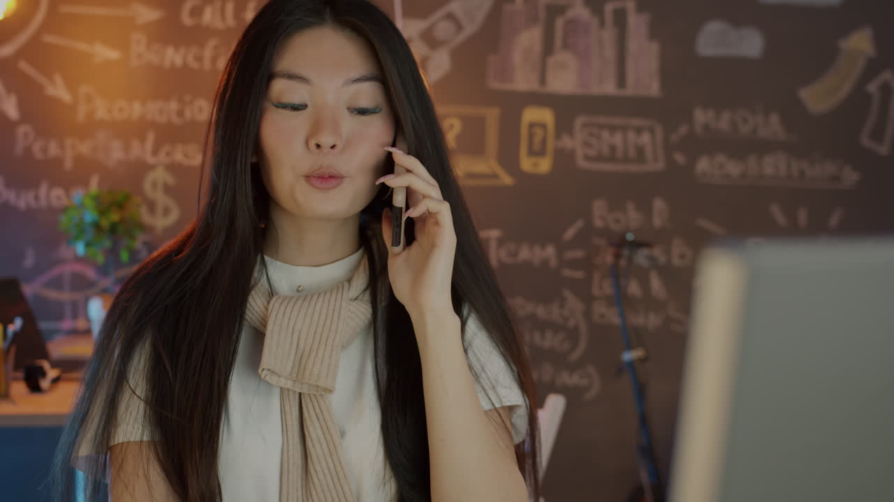 Asian businesswoman talking on phone and working on laptop in office