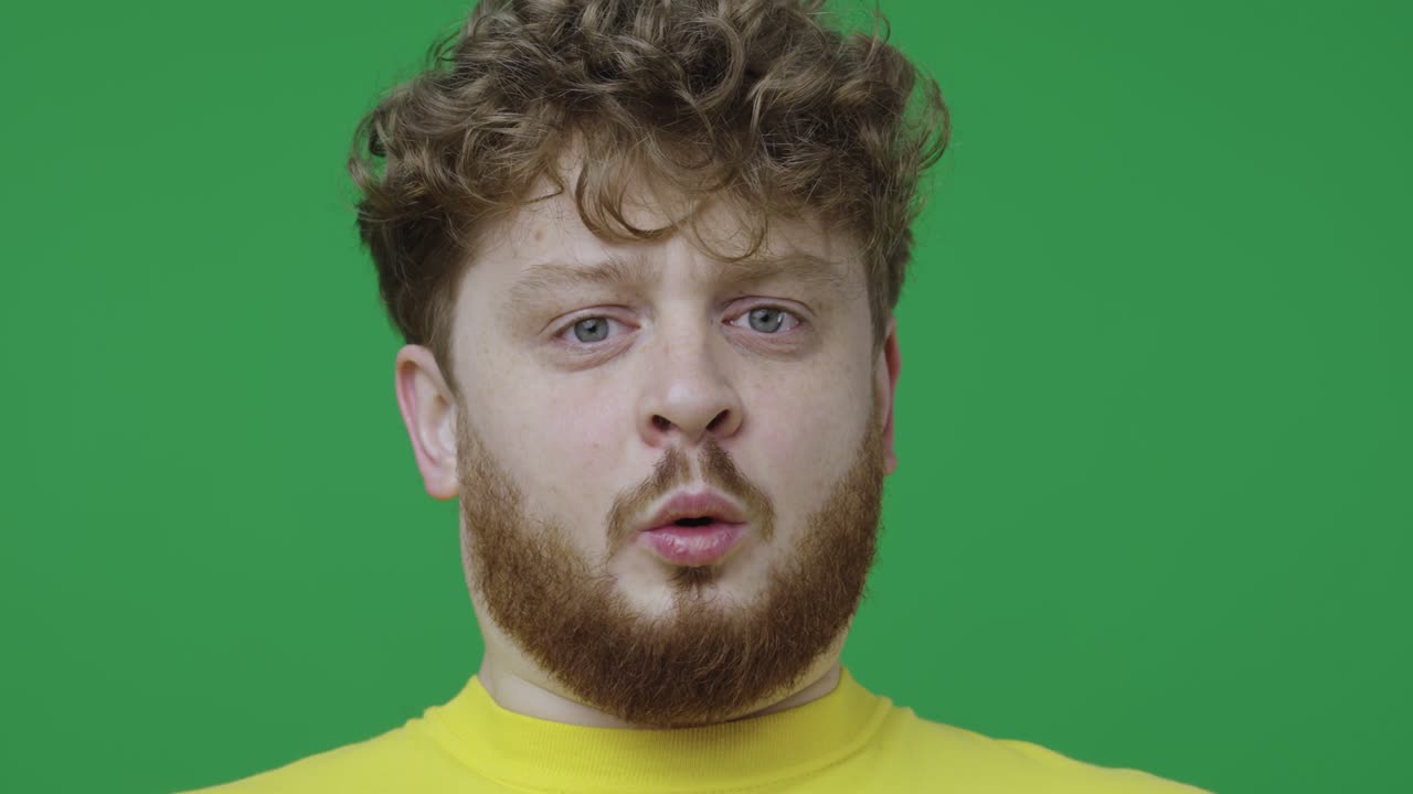 retrato de un hombre mirando a la cámara con sorpresa y conmoción. hombre pelirrojo con cabello rizado y pecas posando en pantalla verde en el estudio. primer plano. cámara lenta lista 59.97fps