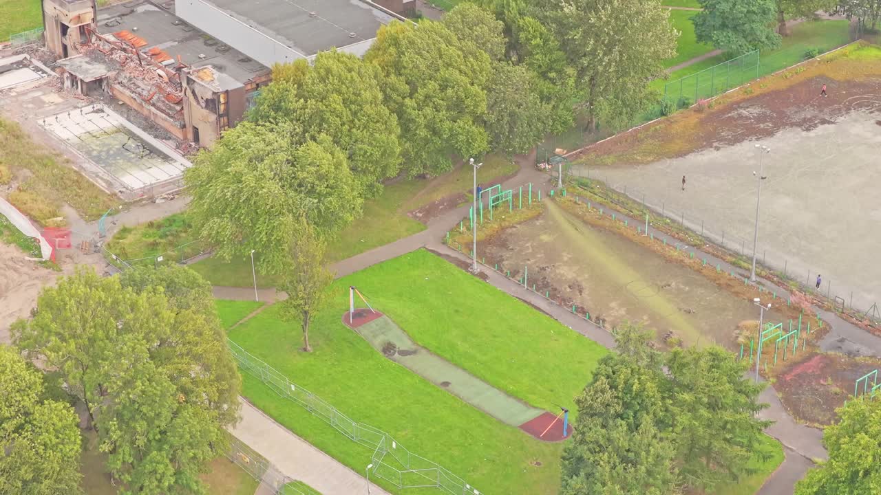 Aerial view of a compact neighborhood play area in Salford—featuring zipline or aerial-runway play equipment, grass, and walking paths near Irwell Riversi