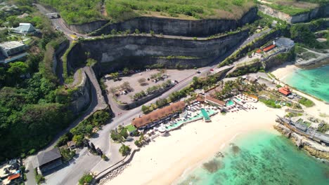 Descenso-Aéreo-Que-Revela-Exóticos-Clubes-De-Playa-En-La-Playa-De-Melasti,-Sinuoso-Camino-Empinado-Desde-El-Acantilado-Hasta-El-Resort-Ungasan-De-La-Playa-De-Melasti-En-Uluwatu,-Bali.