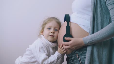 girl puts headphones on mum large belly and listens to baby