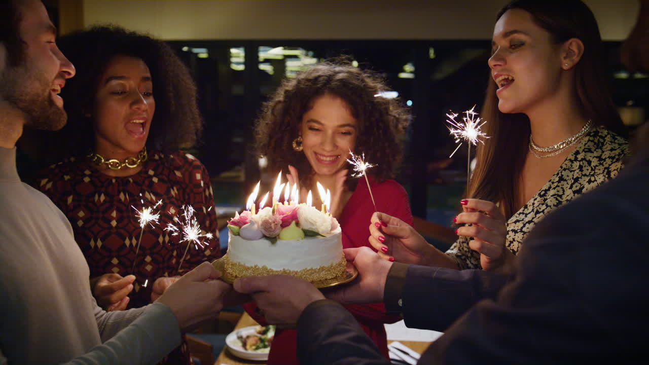amigos multiétnicos celebran su cumpleaños en una cafetería. quemando velas en un pastel sorpresa