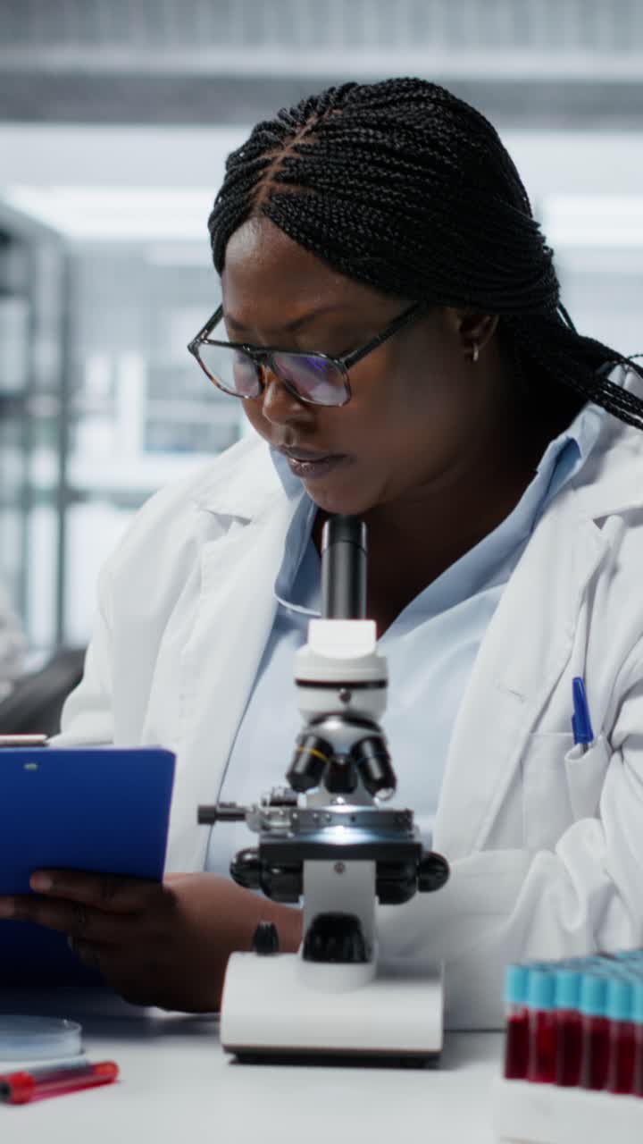 Video verticale: esperto di laboratorio medico che usa il microscopio, annotando i risultati della ricerca