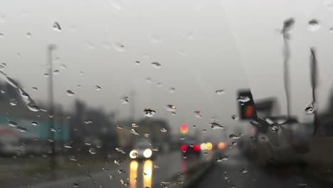 bad rainy weather with raindrops sliding down on windscreen and blurred lights of car traffic in background