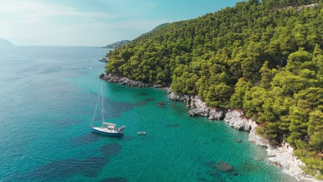 un velero anclado cerca de una frondosa costa boscosa con aguas cristalinas de color turquesa