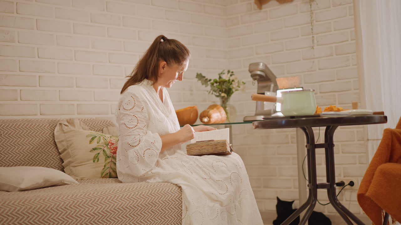 Cozy living room baking pumpkin pie with vintage mixer and soft light, white woman kneads crust and tests filling while seated on sofa beside brick wall scene shows pumpkins on table, recipe notes