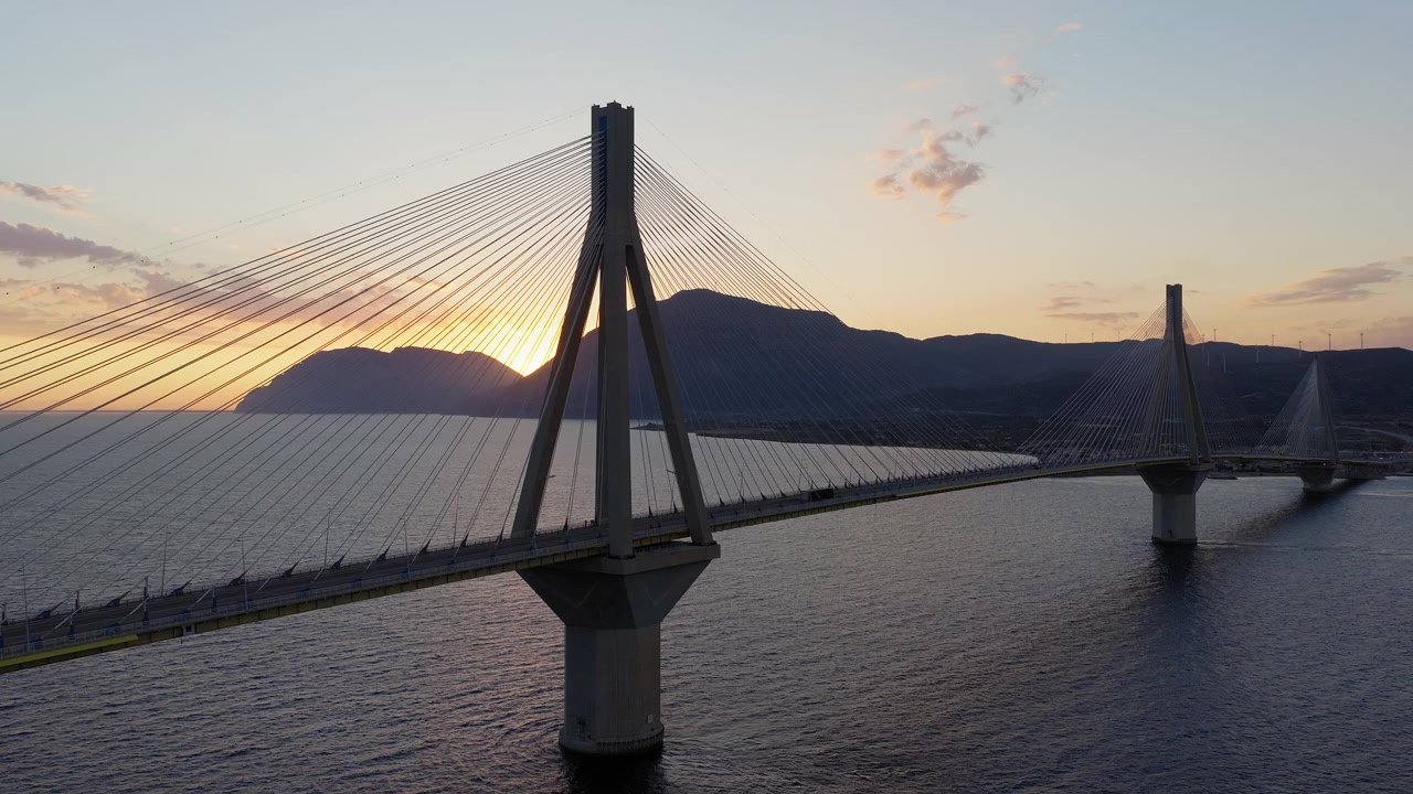 Ponte Rio-Antirrio con tramonto sul Golfo di Corinto, drone che si sposta a sinistra mentre la luce del sole illumina i cavi di supporto