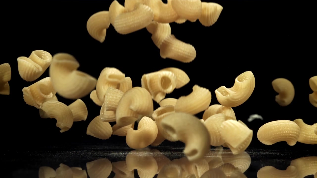 Pasta maccheroni secca che cade al rallentatore su sfondo nero.