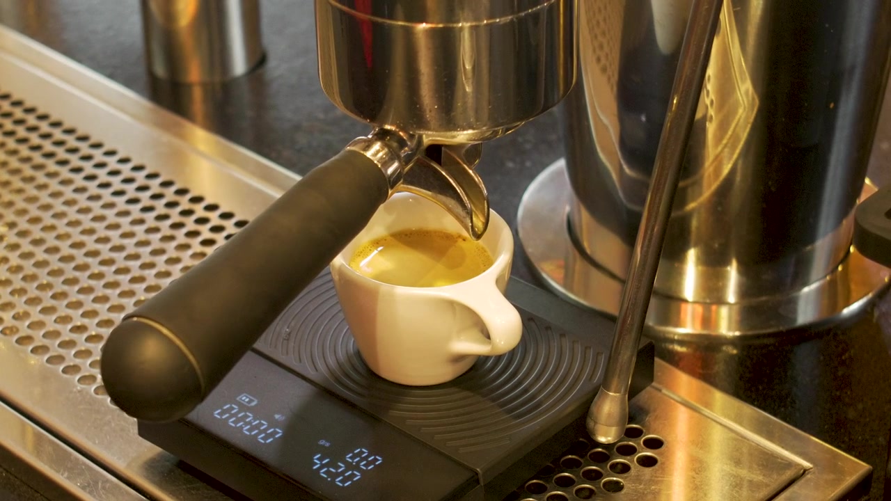 Preparazione artigianale di espresso con bilancia digitale e tazza bianca presso una postazione da barista professionale.