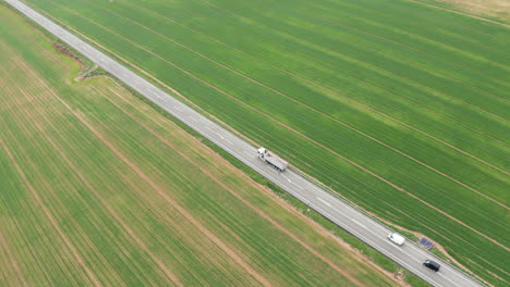 Lastwagen-Und-Autos-Fahren-Auf-Einer-Straße-Vorbei,-Grünes-Grasfeld,-Spanische-Agrarwirtschaft,-Ackerland