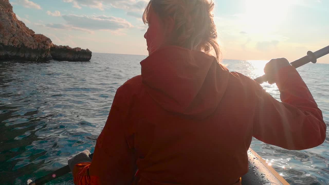 일몰의 활기찬 색채 가운데, 뒤에서 가까이 찍은 사진은 크로아티아에서 카야크를 타는 소녀를 포착합니다. 자연의 아름다움과 모험적인 정신을 혼합합니다.