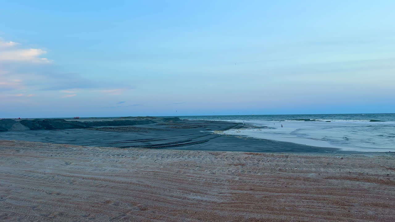 Wide panning view, excavator and pier near beach sand replenishment